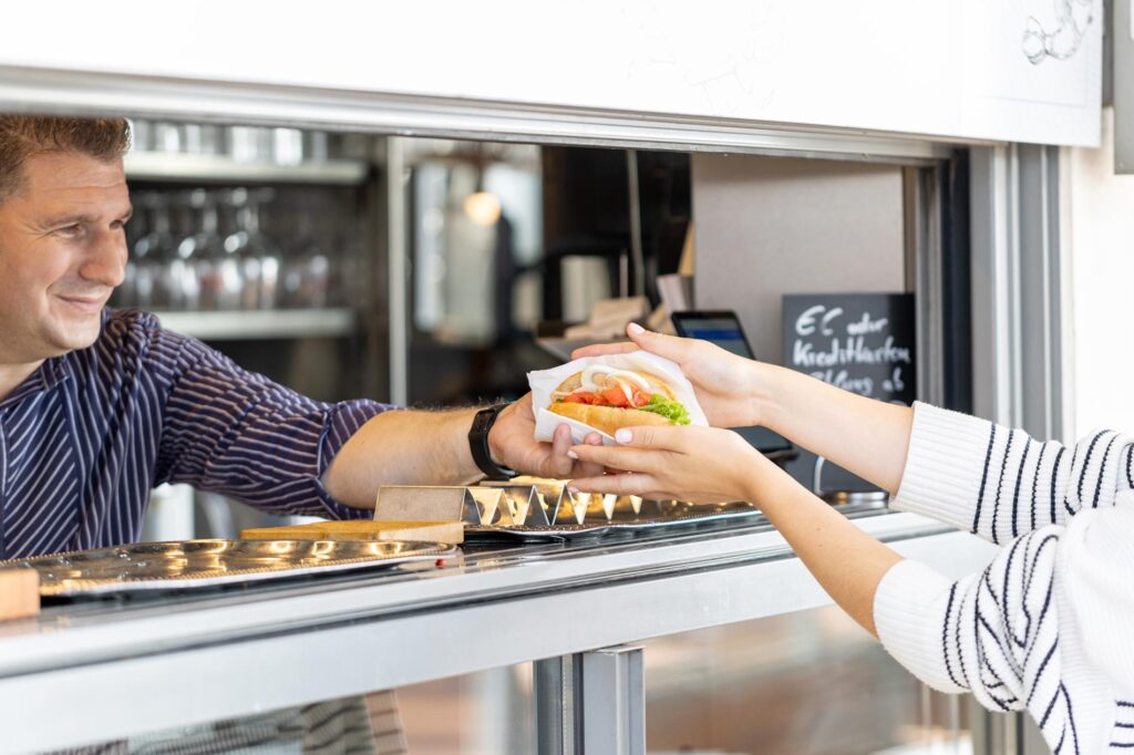 Fischbrötchen König Ansicht von Angestelltem der Gast ein Seelachsbrötchen über den Tresen reicht